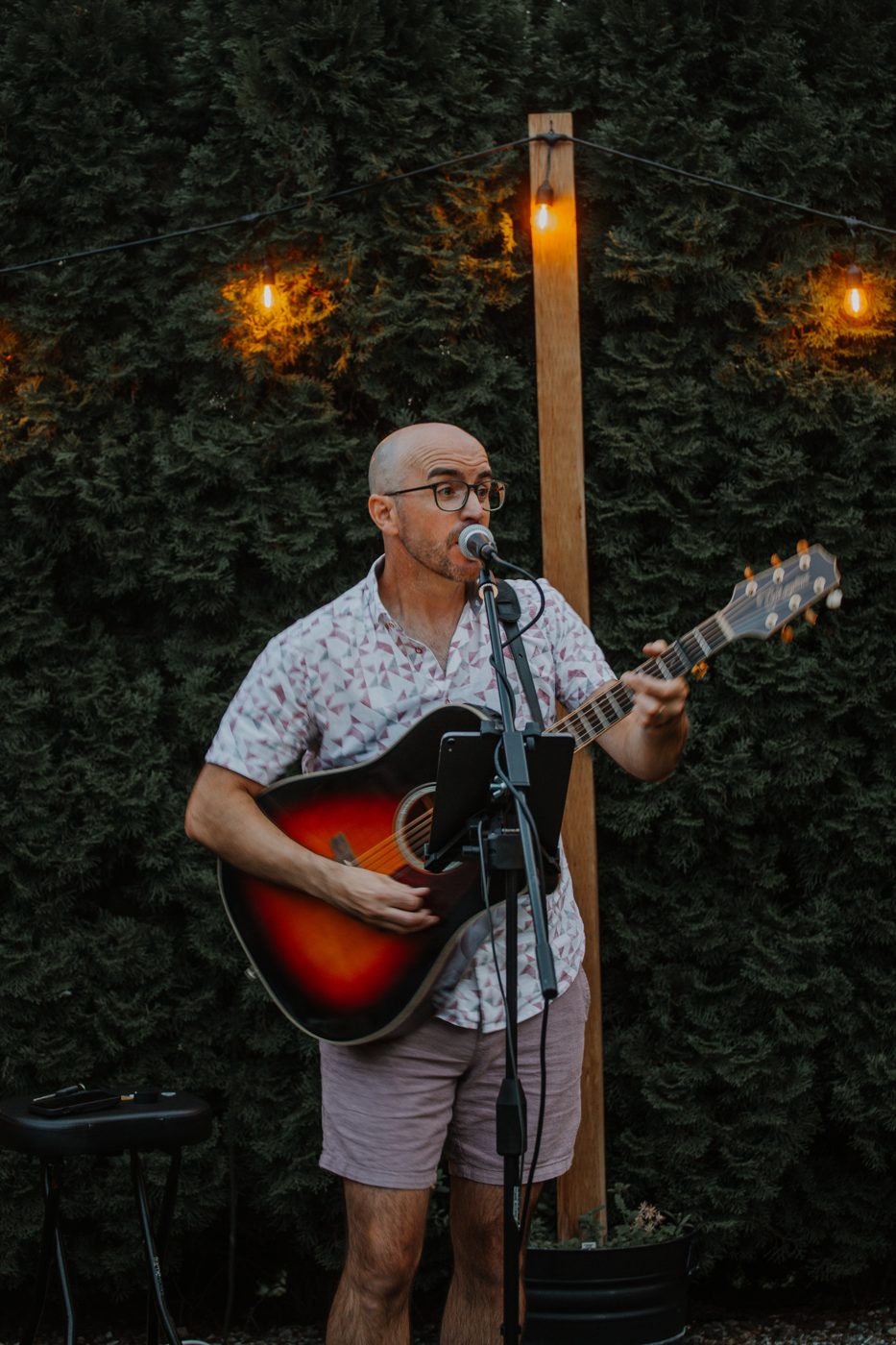 Colin singing at an evening backyard party, string lights behind