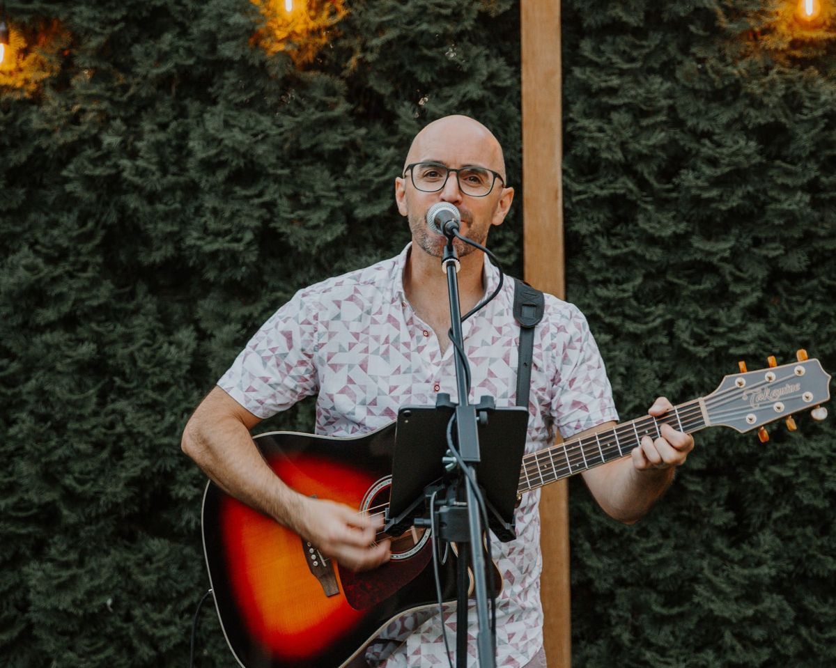 Colin singing at an evening backyard party under string lights