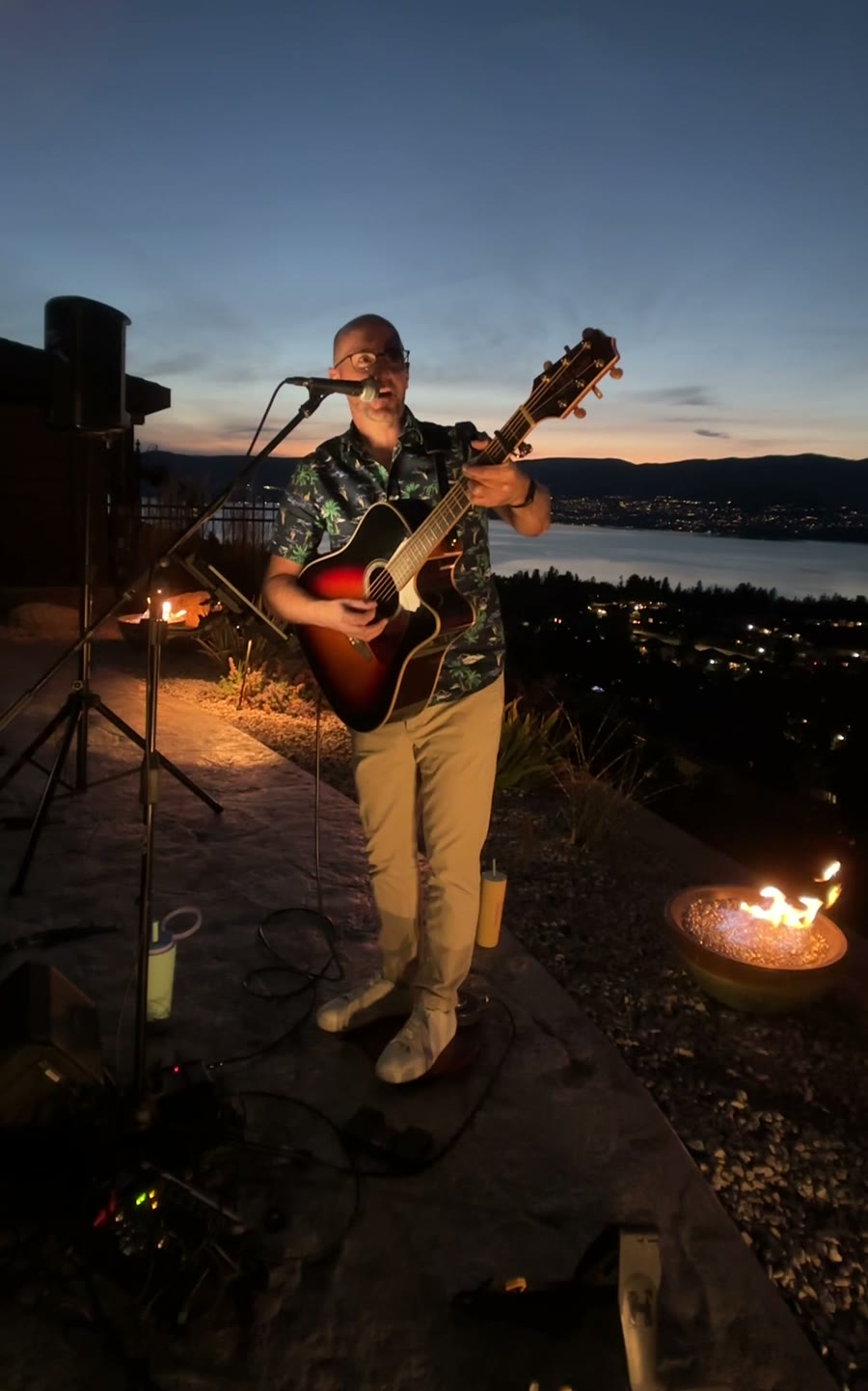 Colin playing on a terrace above Okanagan Lake at dusk, a fire bowl glowing beside him