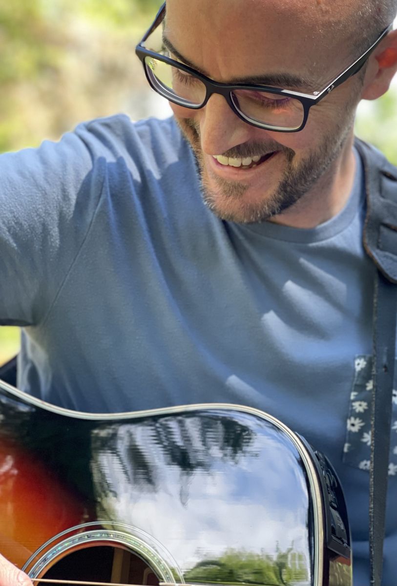 Colin grinning down at his guitar in an orchard