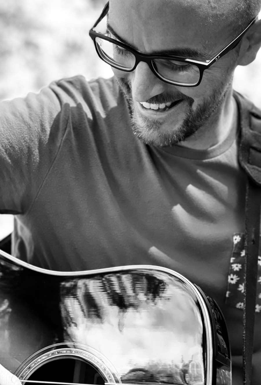 Colin grinning down at his guitar, in black and white